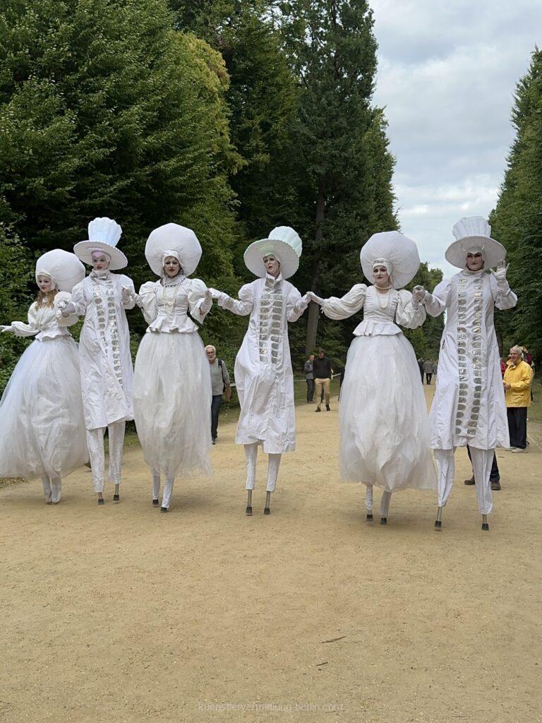 White stilt walkers in historical costumes stride majestically through the guests and greet visitors from afar with an impressive performance